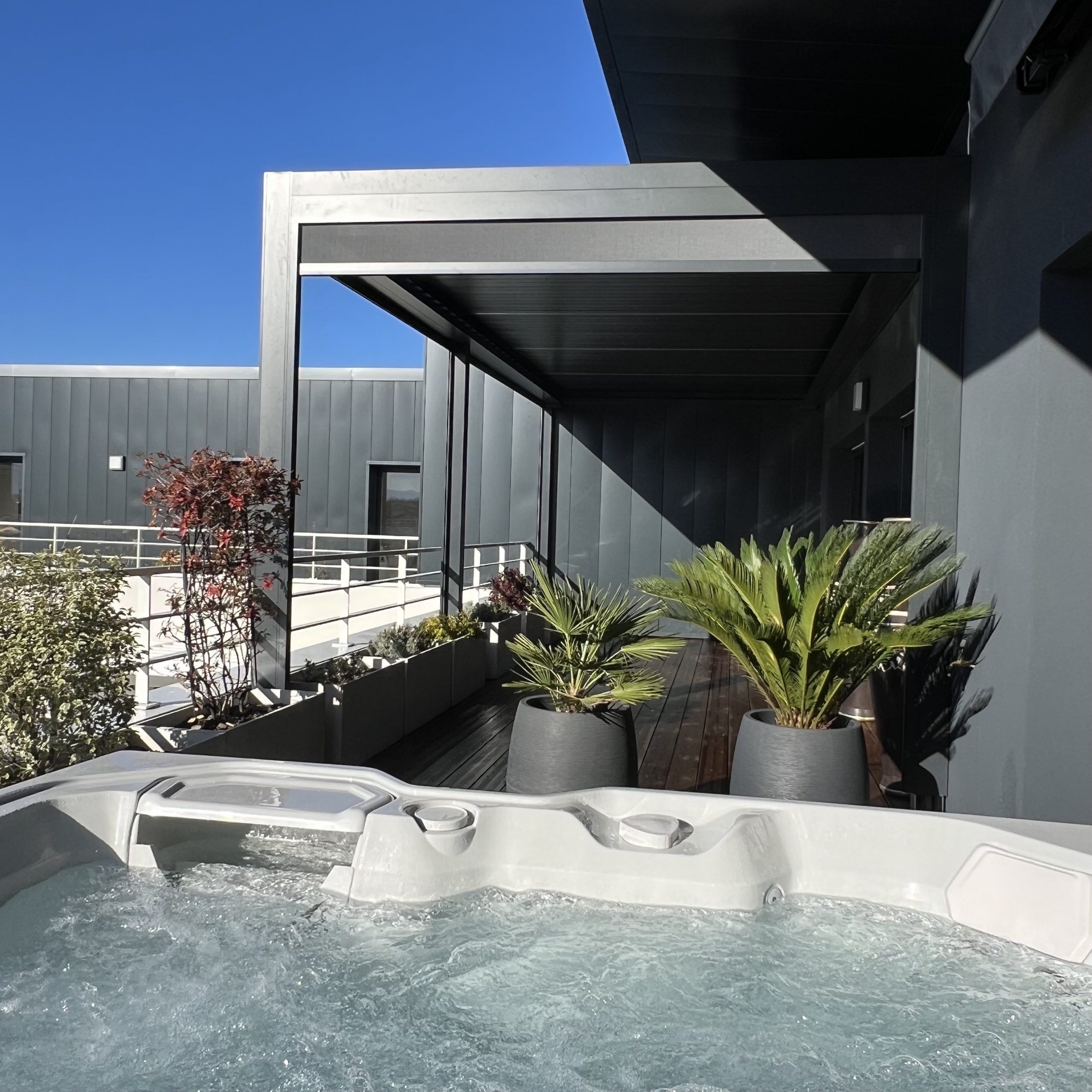 Image d'une pergola bioclimatique rétractable avec jacuzzi et plantes sur un balcon.